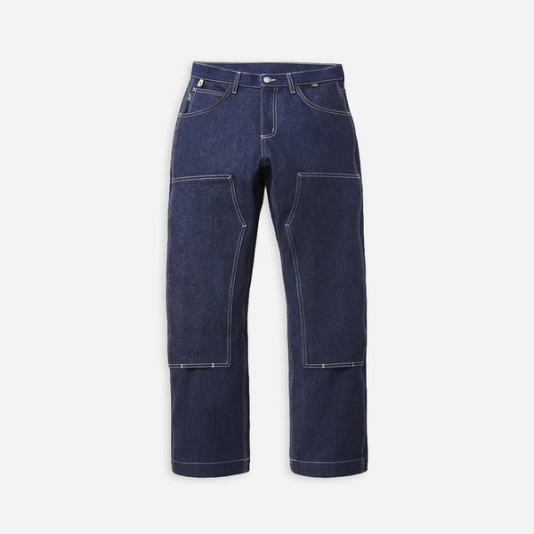 Dark indigo blue denim work pants with large front cargo pockets and contrast light stitching, shown flat against a light gray background.