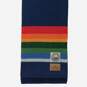 Pendleton - Pendleton National Park Twin Blanket - Crater Lake Navy - A folded navy blue wool scarf with horizontal rainbow stripes in red, orange, yellow, green, blue, and white, featuring a Pendleton brand patch and a circular mountain emblem. - Alternative View 1
