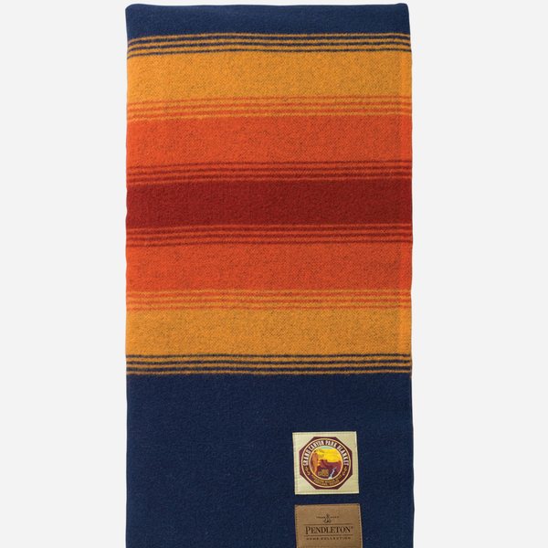 A Pendleton wool scarf with a striped pattern in navy blue, orange, red, and yellow, featuring a brand patch and label near the bottom.