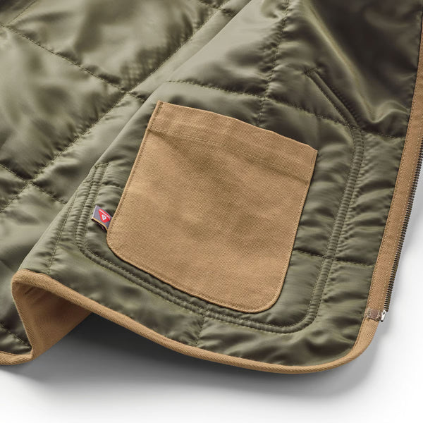 Close-up of a green quilted jacket with a brown pocket on a white background