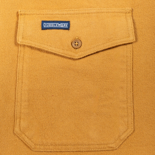 Close-up of a mustard yellow suede or suede-like fabric pocket with a flap closure, a single button, and a visible Doubleware label.
