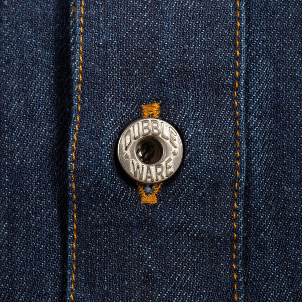 Close-up of a dark blue denim button-up shirt featuring orange contrast stitching and a silver metal button engraved with 'DUBBLEWARE'.
