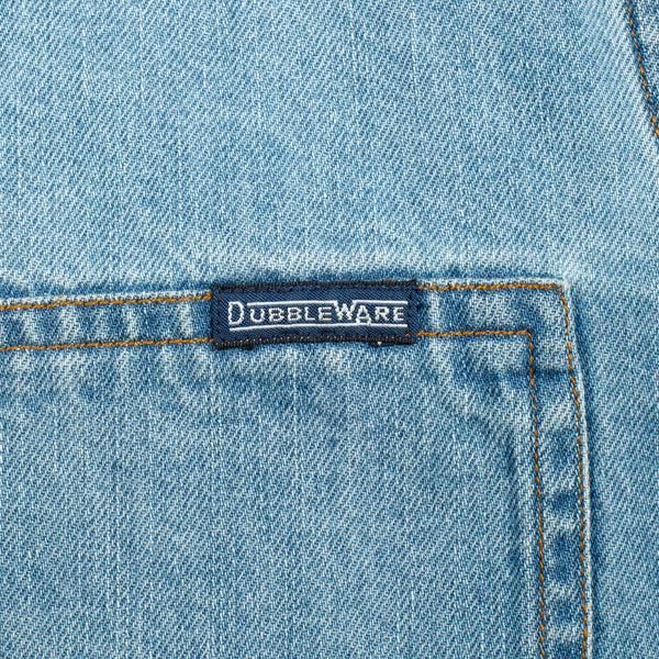 Close-up of a light blue denim garment showing a front pocket with contrast stitching and a small dark brand label reading Dubbleware.