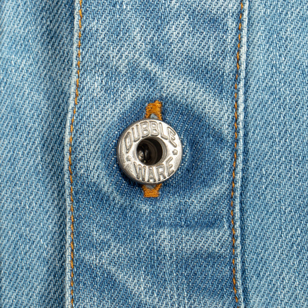 Close-up of a light blue denim garment with orange contrast stitching and a silver metal button embossed with the brand name 'CUBBLEWARE'.