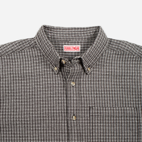 Close-up of a button-down shirt collar with a small red and white Bubbleware neck label, featuring a fine brown and beige checkered pattern.