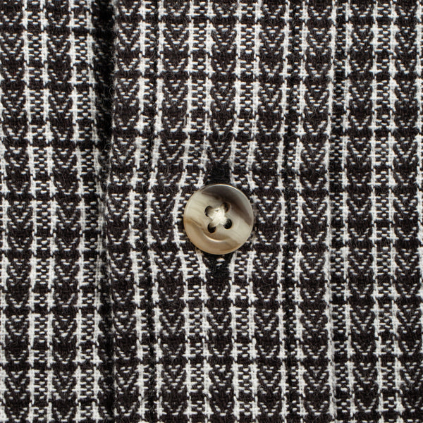 Close-up of a black and white woven fabric with a repeating geometric pattern and a single round metallic button near the center.