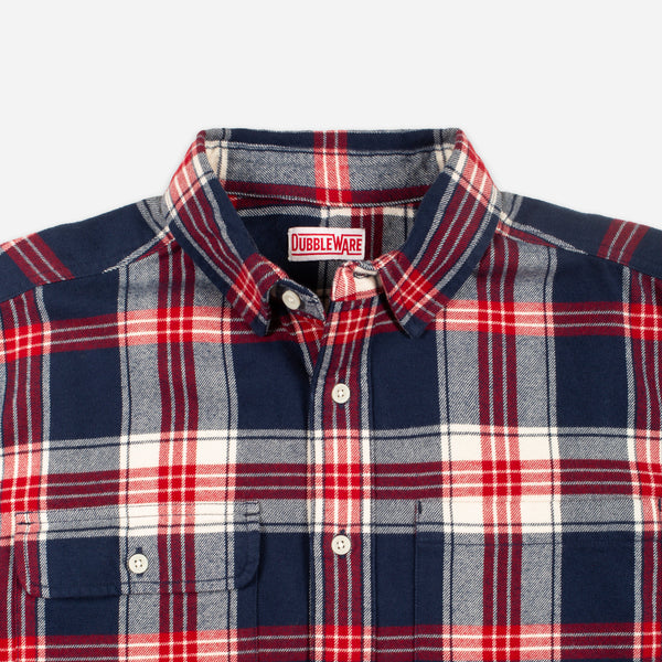 A close-up of a Doubleware plaid button-down shirt in navy blue, red, and white, showing the collar, buttons, and chest pocket.