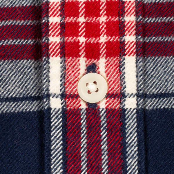 Close-up of a plaid fabric with red, navy, and white stripes, featuring a single cream-colored button.