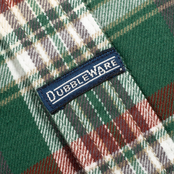 Close-up of a green plaid fabric with red, white, and gray stripes, featuring a navy blue woven label with the brand name 'DUBLEWARE' in white.