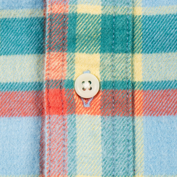 Close-up of a plaid fabric with a light-colored four-hole button, showing intersecting stripes of teal, light blue, yellow, and coral red.