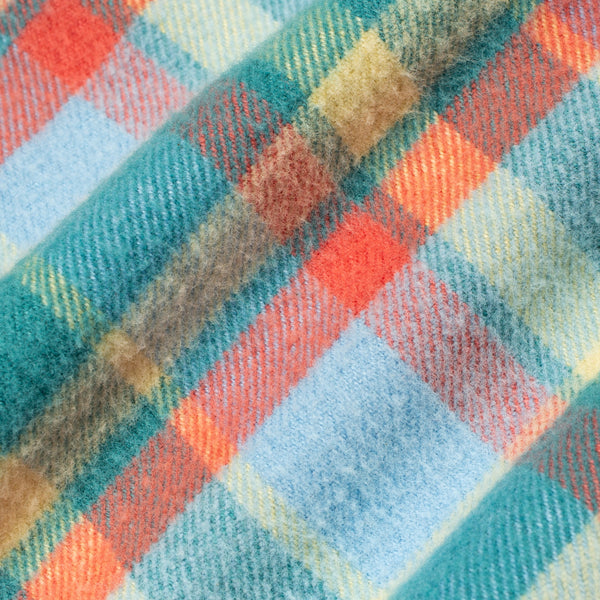 A close-up of a plaid fabric pattern with diagonal stripes in teal, light blue, orange, beige, and brown.