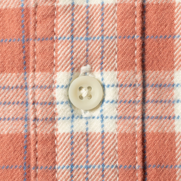 Close-up of a plaid fabric with a white button, showing a pattern of coral pink, white, and light blue stripes.