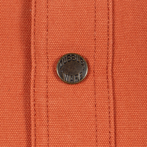 Close-up of an orange woven fabric with vertical stitched channels and a round dark metal button embossed with the brand name 'DUBBLE WARE'.
