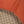 Load image into Gallery viewer, Close-up detail of a garment corner showing a rust-orange woven fabric body meeting a brown, beige, and black plaid lining.
