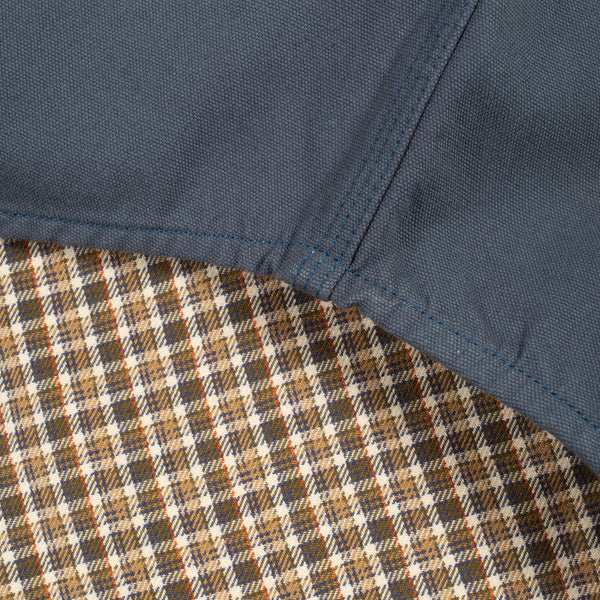 Close-up detail of a garment showing a dark slate blue fabric panel stitched over a brown, beige, and white plaid lining.