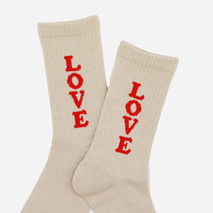 Rostersox - LOVE SOCKS - BEIGE - A pair of cream-colored ribbed crew socks with the word 'LOVE' knitted vertically in red on each sock, displayed against a light gray background. - Alternative View 1