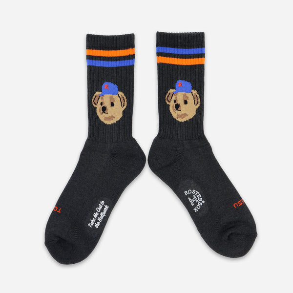 A pair of dark charcoal gray crew socks featuring a cartoon dog face wearing a blue cap on the upper leg, with blue and orange stripes near the cuff. White text on the toes reads 'Tired of Being Sh*tty'.