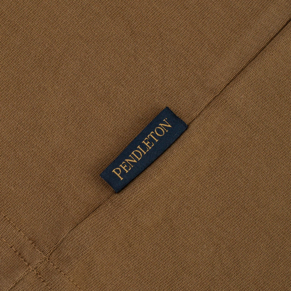 Close-up of a brown woven fabric with a small dark navy label stitched on it, printed with the brand name PENDLETON in gold lettering.
