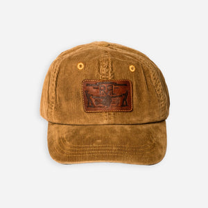 Double RL By Ralph Lauren - RRL Leather Patch Corduroy Trucker Cap Tan - A brown corduroy baseball cap with a brown leather patch on the front featuring a stylized eagle logo, photographed against a light gray background. - Main Front View