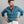 Load image into Gallery viewer, A man with a reddish beard wearing a textured blue long-sleeve henley shirt and off-white pants, posing with hands on hips against a solid gray studio background.
