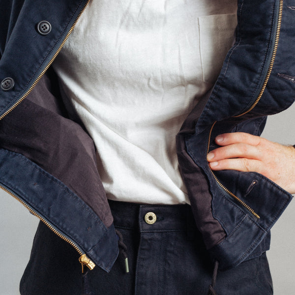 Close-up of a person wearing a dark navy jacket over a white shirt and dark navy pants, with the jacket open to show the interior lining and zipper details.