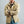 Load image into Gallery viewer, A man wearing a tan canvas button-up shirt jacket over a green shirt, blue jeans, and a tan baseball cap, standing against a plain gray studio background.
