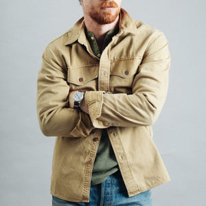 Double RL By Ralph Lauren - Officer's Long Sleeve Sports Shirt - Faded Tan - A man wearing a tan canvas button-up shirt jacket over a green shirt, blue jeans, and a tan baseball cap, standing against a plain gray studio background. - Alternative View 1