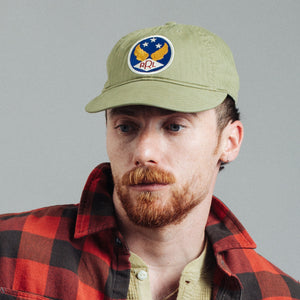 Double RL By Ralph Lauren - RRL Garment-Dyed Twill Ball Cap Brewster Green - A man wearing an olive green baseball cap with a circular 'APL' eagle patch on the front, paired with a red and black plaid flannel shirt, photographed against a solid gray background. - Alternative View 1