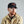 Load image into Gallery viewer, A man with a red beard wearing a black baseball cap with a brown patch and a tan button-up shirt, photographed against a plain light gray background.

